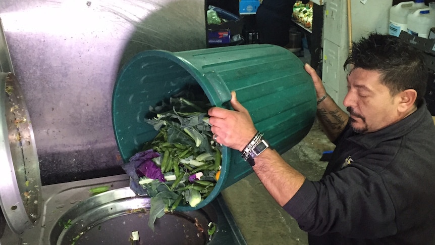 Fruit shop manager Tony Manno pours food waste into a large blender-like machine.