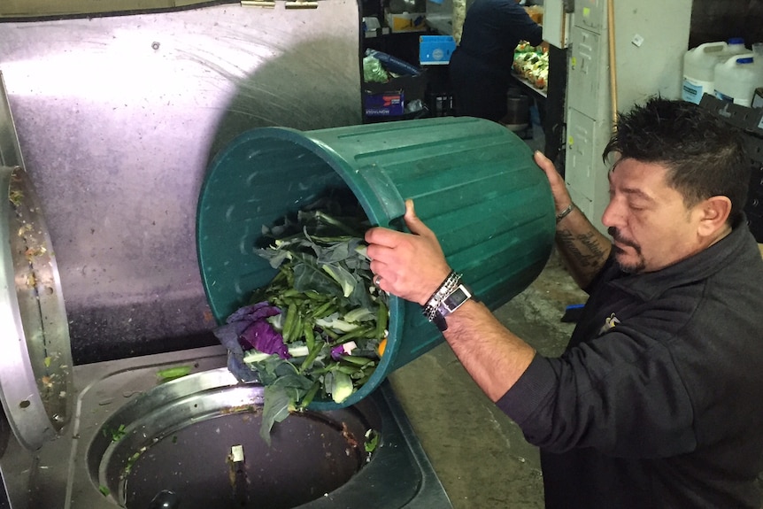 Fruit shop manager Tony Manno pours food waste into a large blender-like machine.