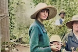 A woman in a hat looks at the camera in a group of hop pickers.