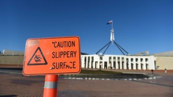 A "caution slippery surface" warning sign is seen outside Parliament House.