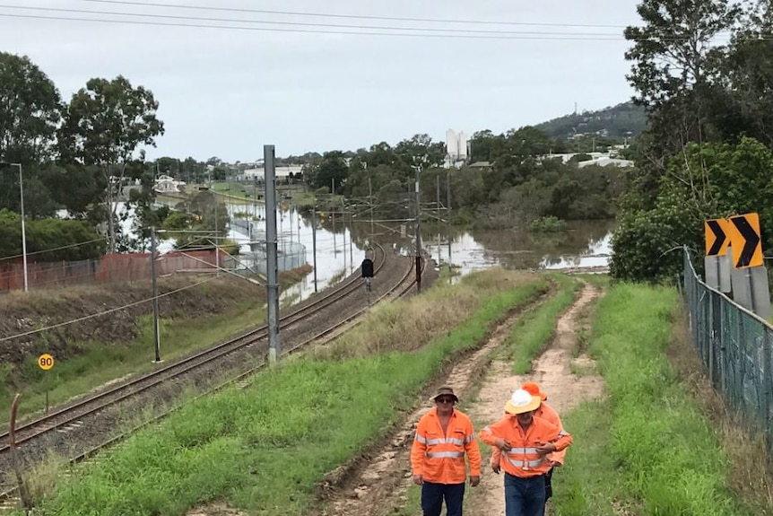 Workers in hi vis gear walk near the Gold Coast railway, cut by floodwaters at Beenleigh.