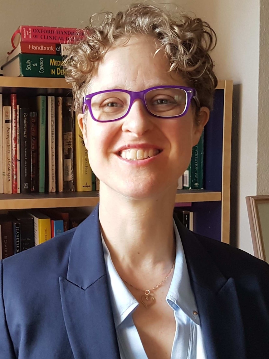 A woman standing in front of a bookshelf smiles into the camera.