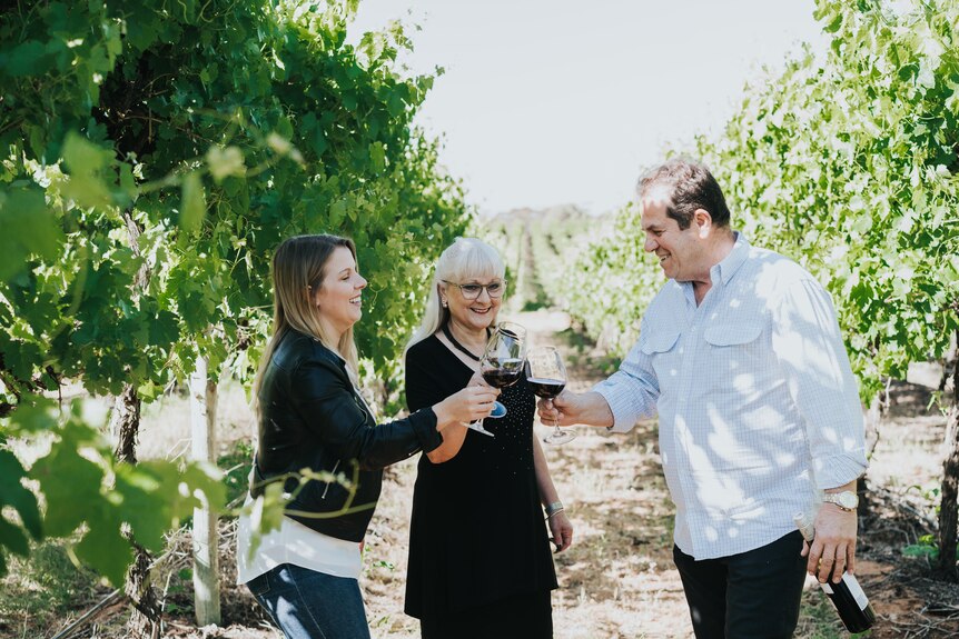  A blonde woman Salena, holds toasts with a glass of wine in a vineyard with blonde mum Sylvia and Italian father Bob.