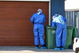 Two people in hazmat suits looking into a green rubbish bin.