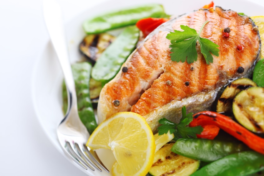 A salmon steak sitting on a bed of grilled vegetables.