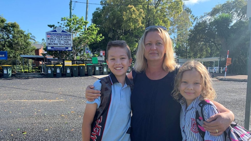 Concerned parent Kylie Rose hugs her two children outside the Murwillumbah East Public School.