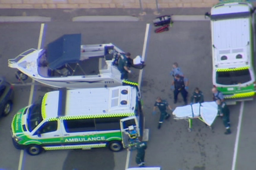 A bird's eye view of a woman's body covered in a sheet on a stretcher being loaded into an ambulance.