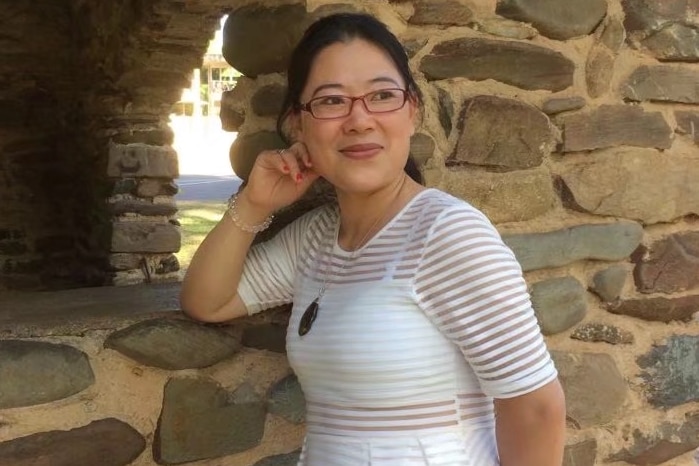 Chen Chi casually poses in front of a building made of stones.