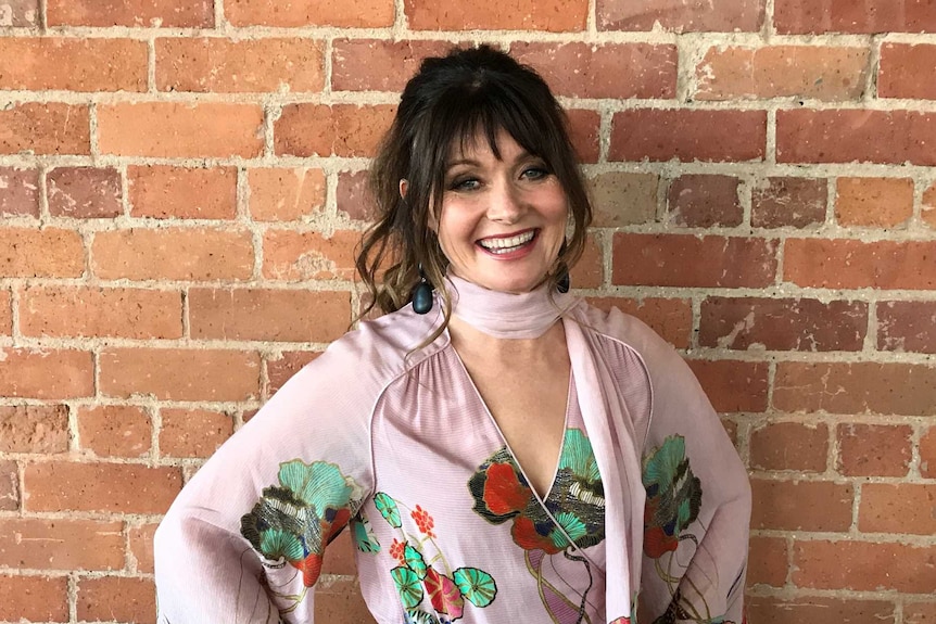 Actor Essie Davis standing against a red brick wall. 