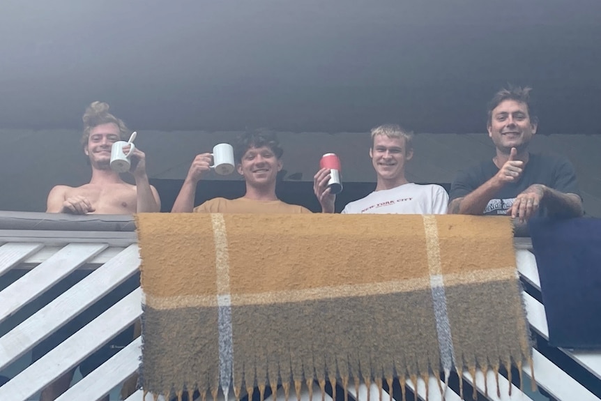 Four backpackers toast their good health by raising their cups on the balcony of Byron Bay's Aquarius Backpackers hostel.