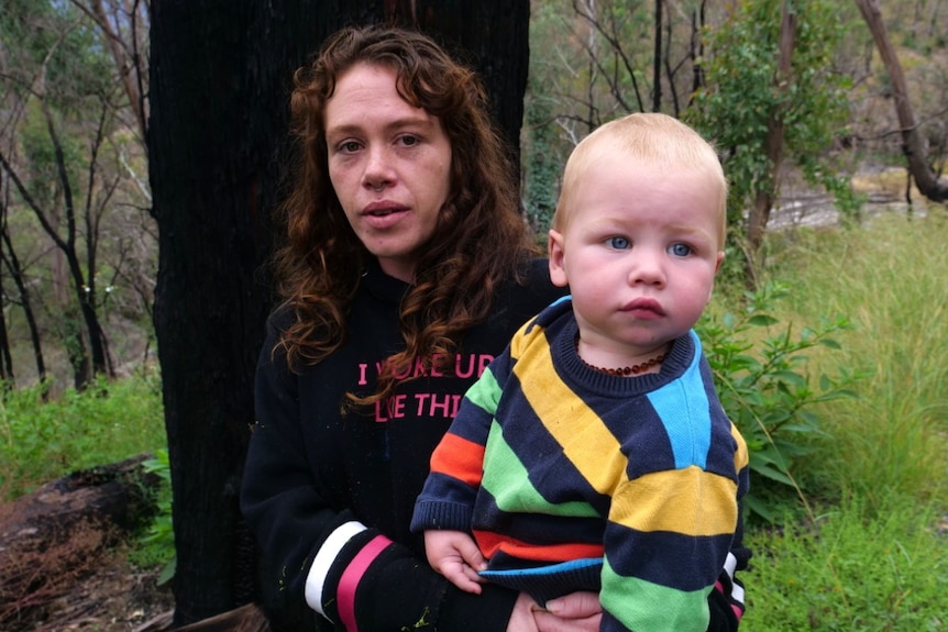 A woman carries a toddler in her arms.