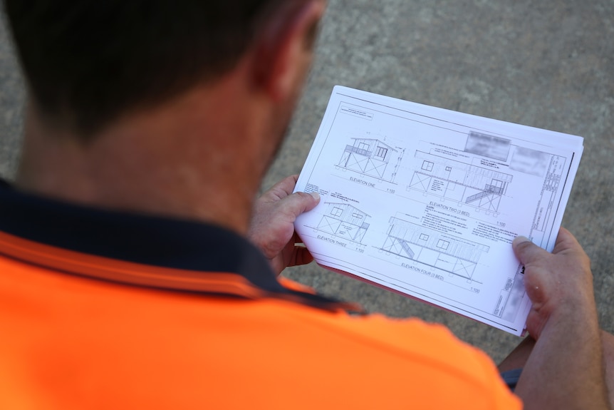 A man in a high vis shirt sits and reads a report containing some building files.