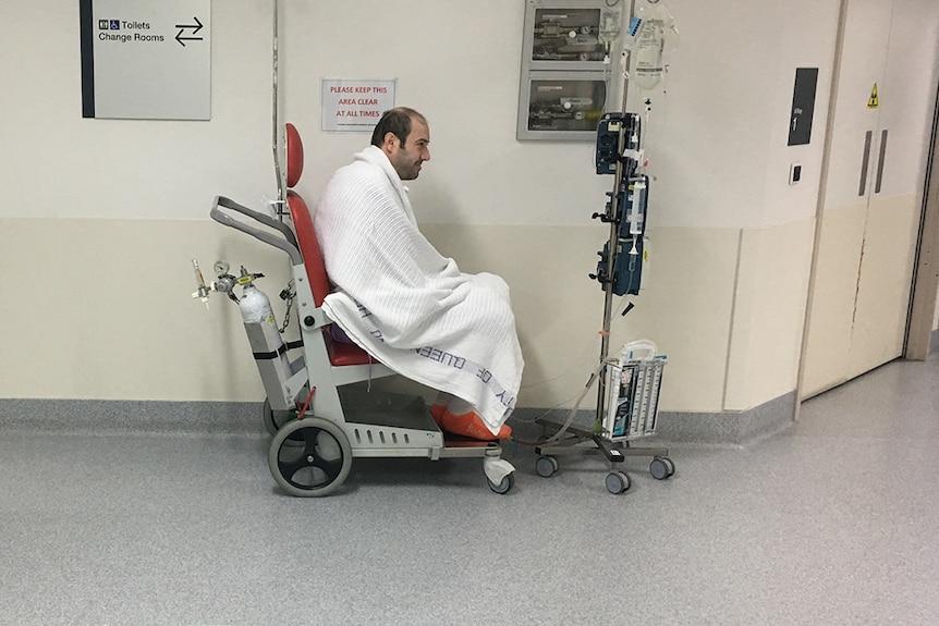 Double-lung transplant patient Jordan Trieger sits alone in a wheelchair in a hospital hallway.