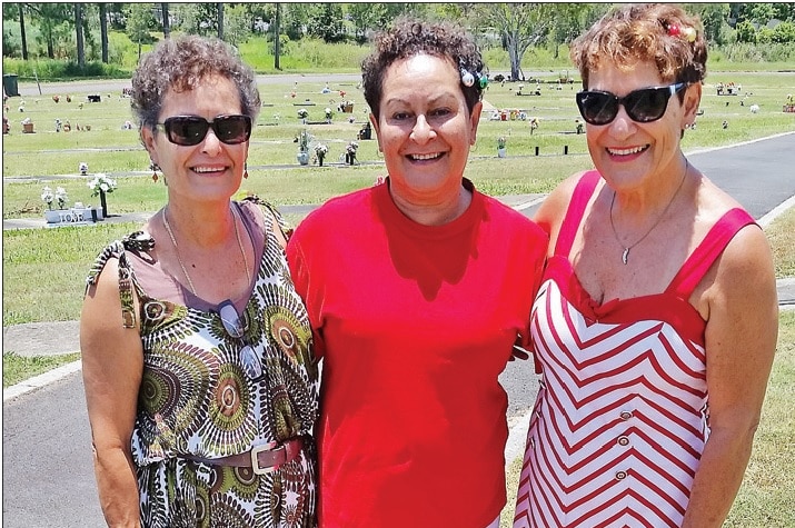 Sisters stand close and smile at the camera.