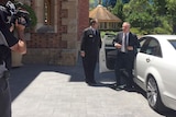Colin Barnett gets out of a white car on the passenger side with a man holding the door and a cameraman filming.
