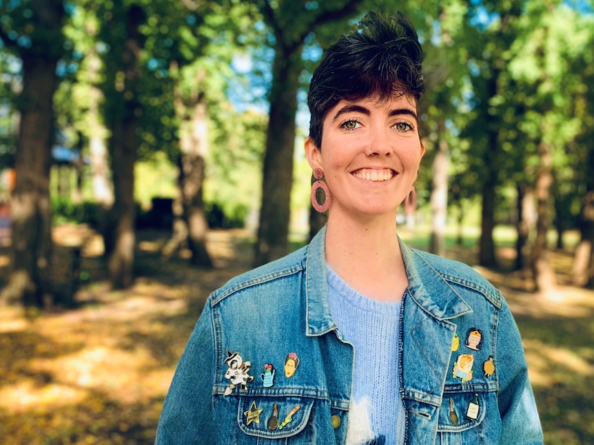 A woman smiles at the camera with trees in the background. 