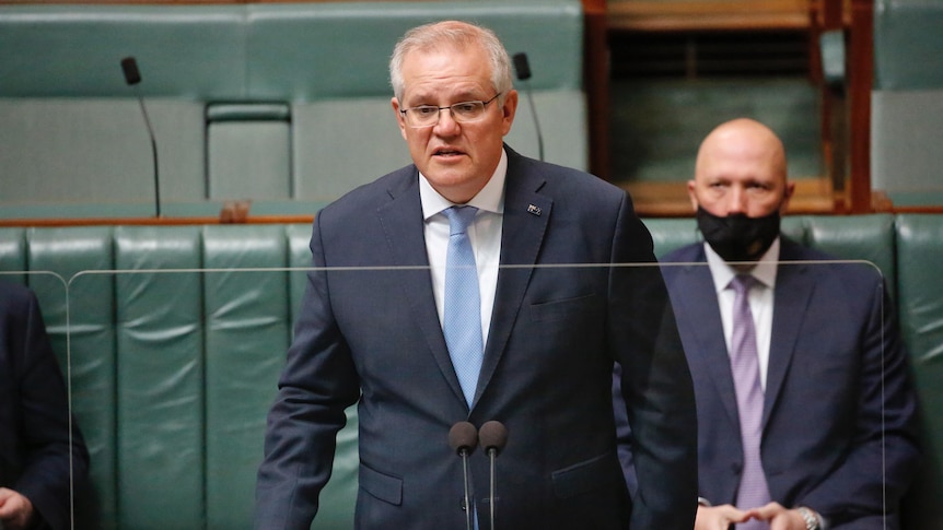 Morrison is standing in a blue suit, a perspex screen in front of him, Peter Dutton behind.