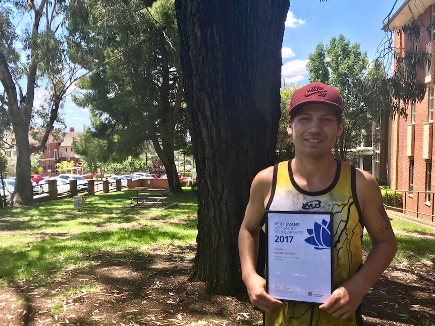 An apprentice smiles holding the certificate marking a scholarship for TAFE study