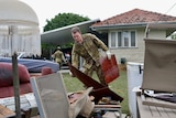 An army officer pics up furniture and puts it on the lawn in front of a house. 