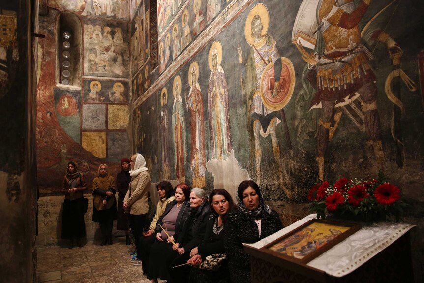 Women sit inside a monastery with painted walls.