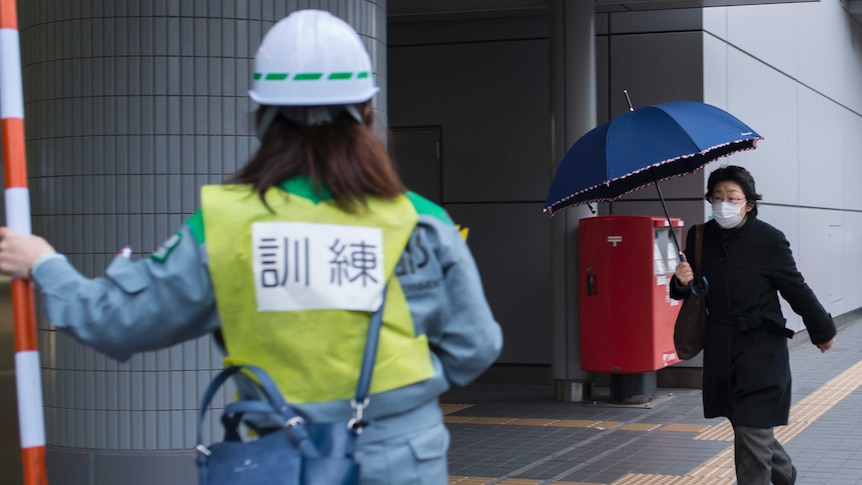 A Japanese woman holding an umbrella walks past Tokyo's subway station during a ballistic missile evacuation drill.