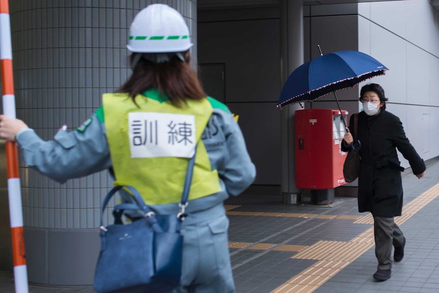 A Japanese woman holding an umbrella walks past Tokyo's subway station during a ballistic missile evacuation drill.