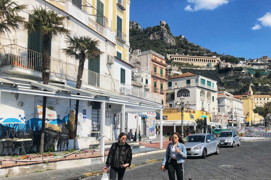 Two women walk down an Italian street holding shopping bags.