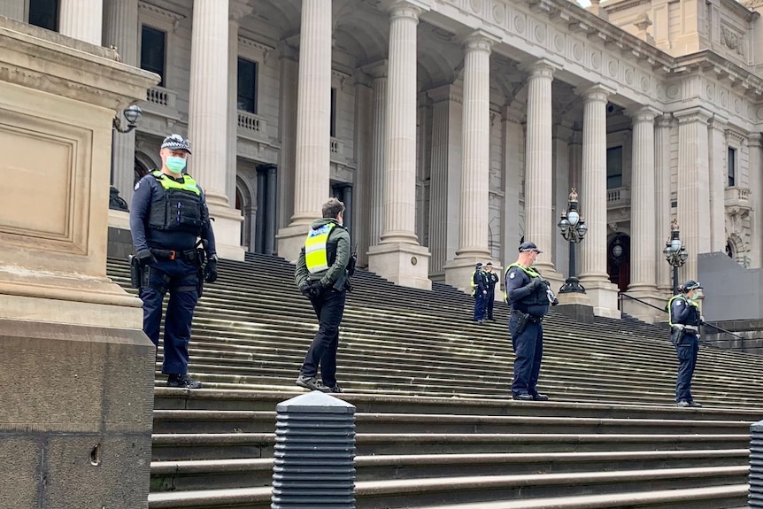 A small number of officers stand on the steps of Victorian Parliament under a clear sky.