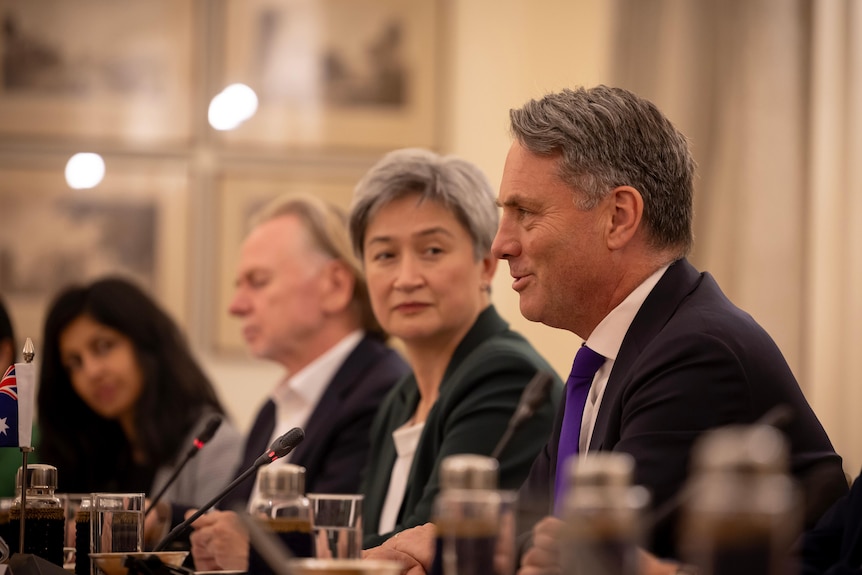 Richard Marles speaks, smiling, at an official meeting while Penny Wong looks on in the background