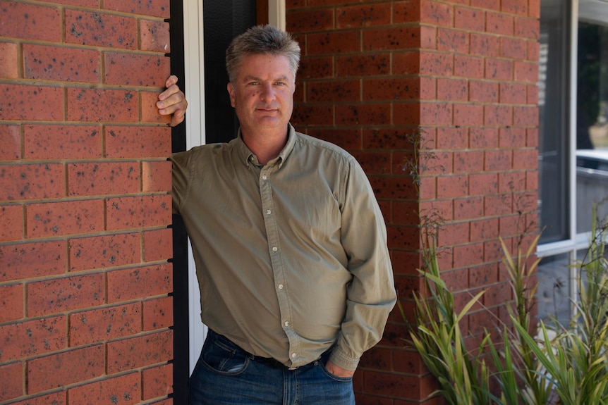 A man with short grey hair leaning against a brick wall