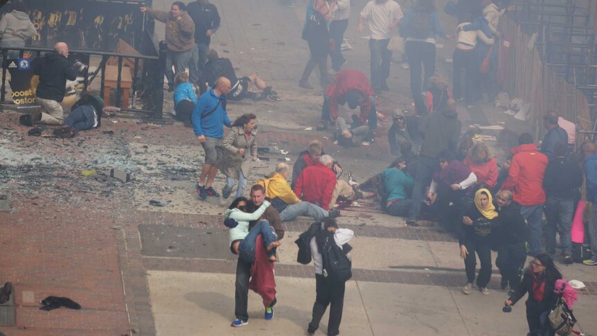 Bystanders rush to help victims of the blast at the Boston marathon as smoke rises.