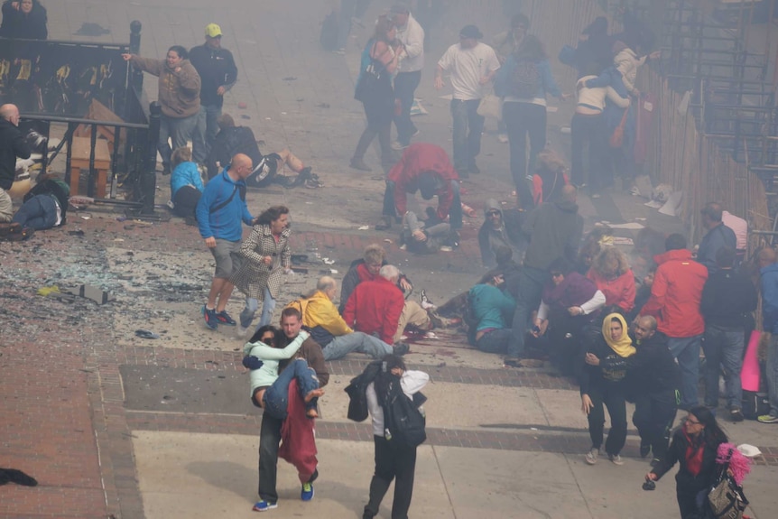 Bystanders rush to help victims of the blast at the Boston marathon as smoke rises.