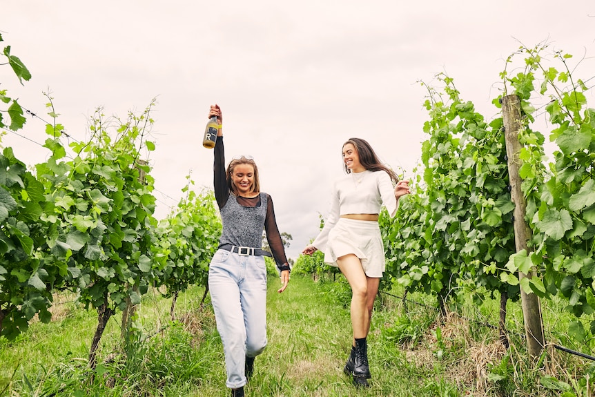 Two girls with a bottle of wine in a luscious vineyard.