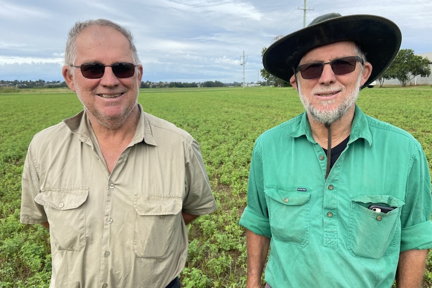 Two men stand smiling to camera in a paddock