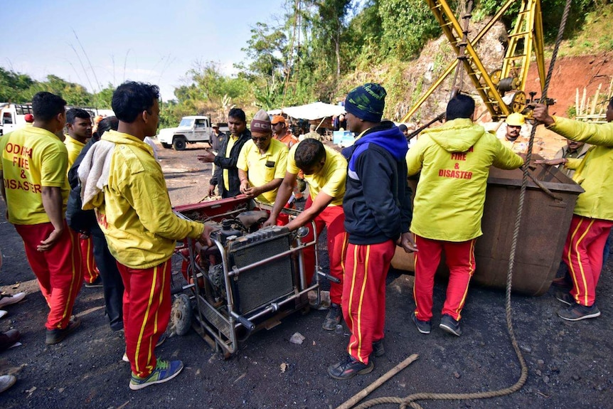 Men in yellow jackets and red pants crowd around a water pump.