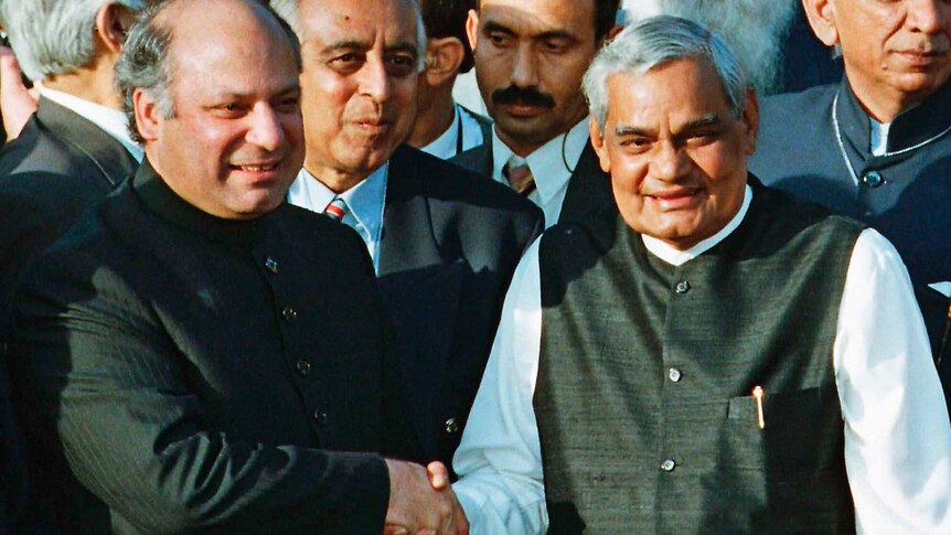 Nawaz Sharif and Atal Bihari Vajpayee shake hands with people standing behind them.