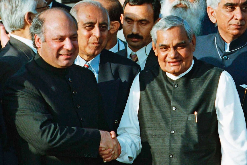 Nawaz Sharif and Atal Bihari Vajpayee shake hands with people standing behind them.