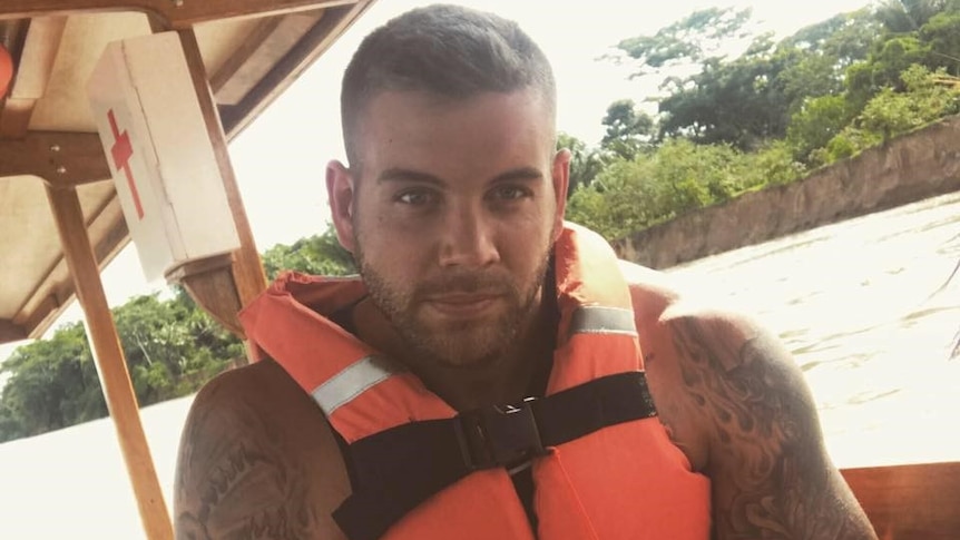 A man sits in a lifejacket on a boat, showing off his tattoos.