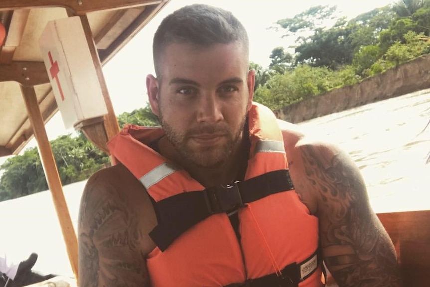 A man sits in a lifejacket on a boat, showing off his tattoos.