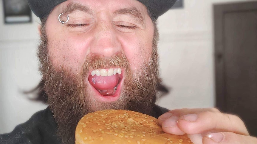 A man holds a McDonald's burger pretending to take a bite.