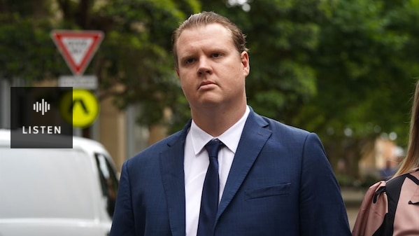 A man with slicked-back hair wearing a dark blue suit . Has Audio.