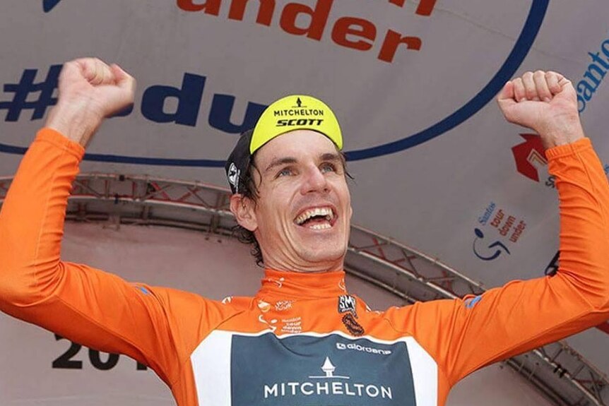 Smiling cyclist raises his arms as he celebrates.