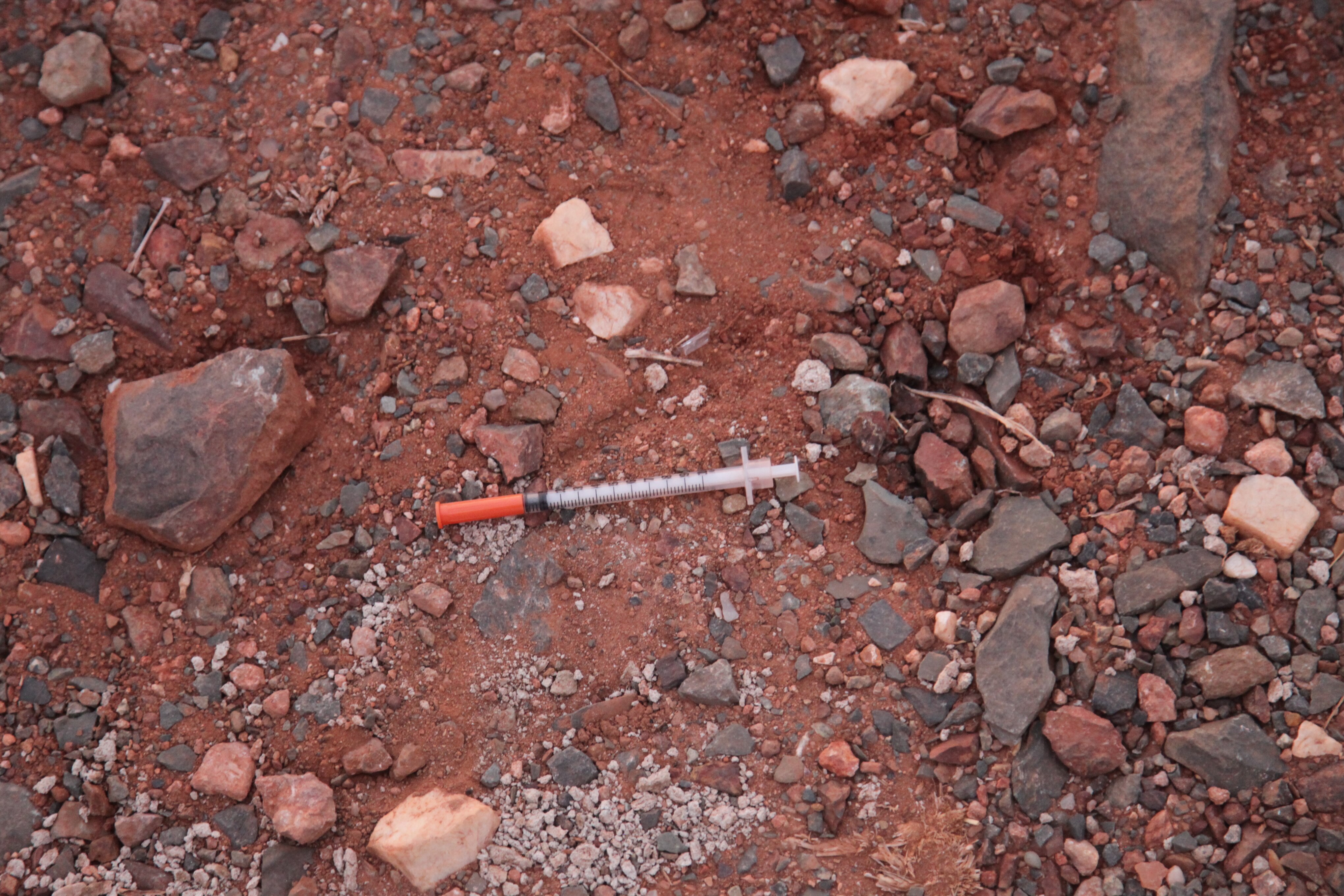 Una aguja yace tirada sobre un suelo hecho de tierra roja y piedras. 