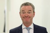 Christopher Pyne smiles while walking down a corridor in a navy suit