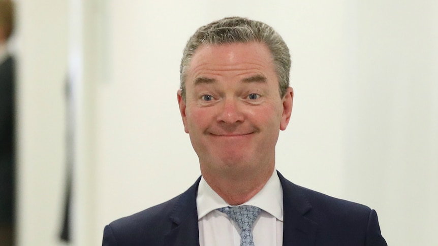 Christopher Pyne smiles while walking down a corridor in a navy suit