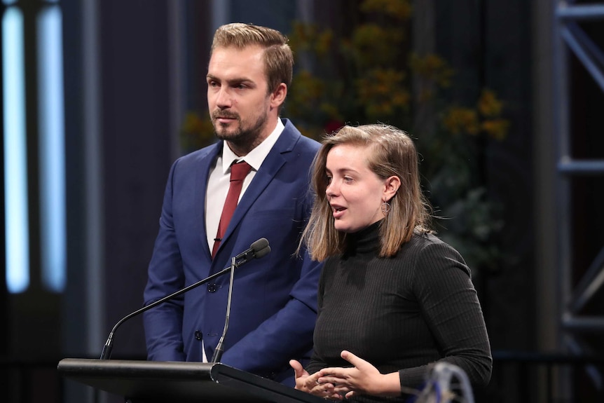 Kurt and Emily Mudie speak at a podium.