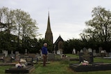 John Temple, a man with white hair and a blue shirt,  in the graveyard of the Anglican Church at Hagley, in Tasmania.