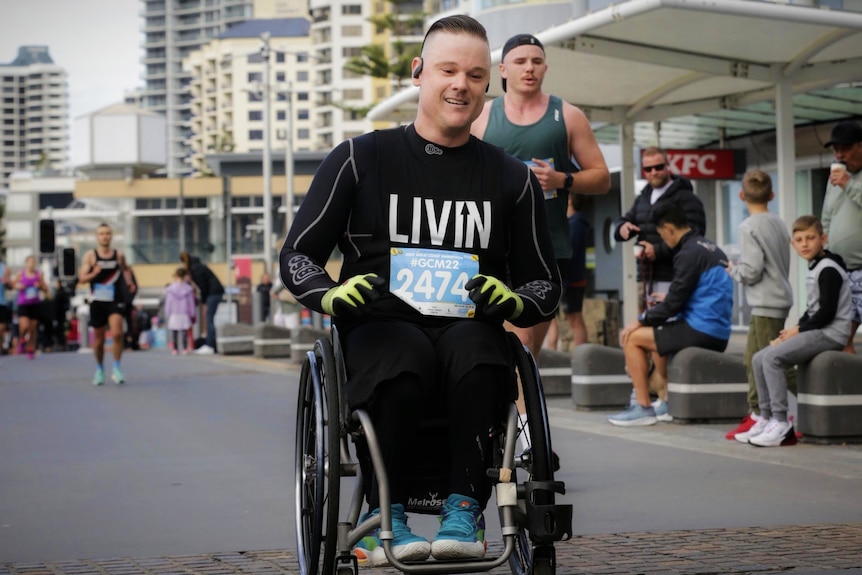 A man in a wheelchair races alongside runners while spectactors watch on 