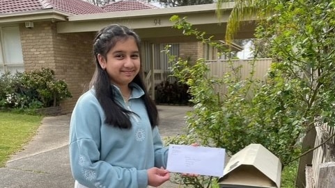 a girl stands with a letter next to her letterbox