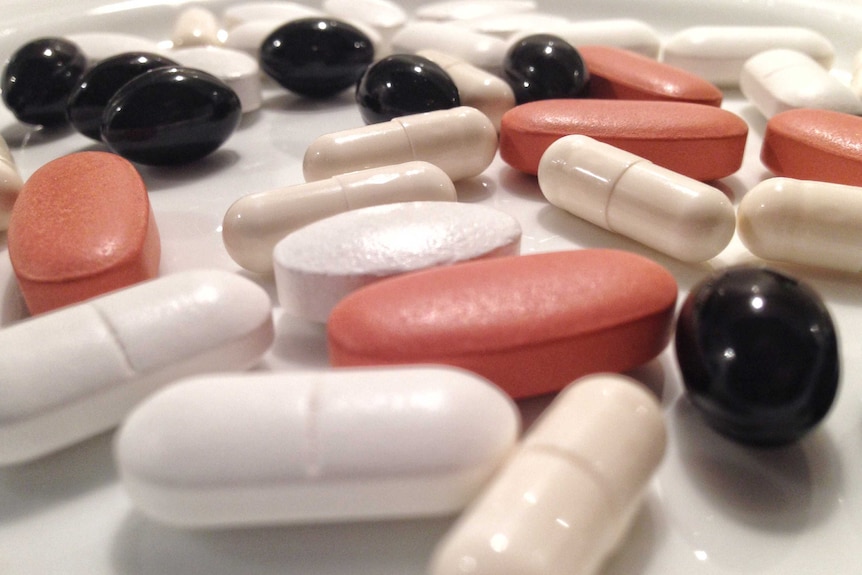 Vitamin pills of different colors scattered on a bench.